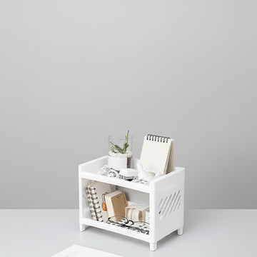 White storage bench with books, a plant, and glasses on a light gray floor.